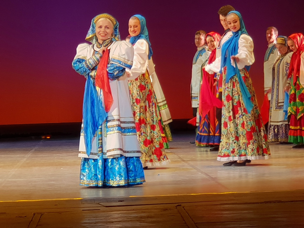 Gruppe von Menschen in bunten, detaillierten traditionellen ukrainischen Kostümen, die auf einer Bühne lächeln.