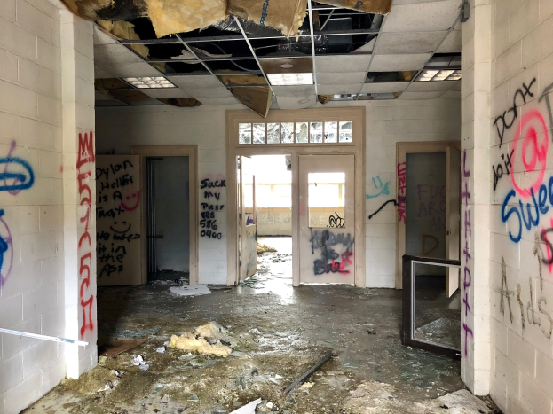Verlassenes Gebäude mit graffiti-bedeckten Wänden und Decke, Schutt auf dem Boden, Türen, Fenster und verstreute Gegenstände im Hintergrund.