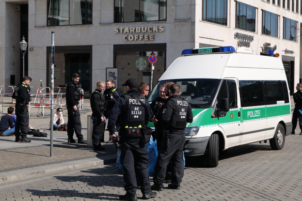 Eine Gruppe von Polizeibeamten vor einem Starbucks-Café mit einem Van auf der rechten Seite und einigen Menschen auf der linken Seite, mit einem Gebäude, einem Schild, einem Lichtmast und einem Zaun im Hintergrund.