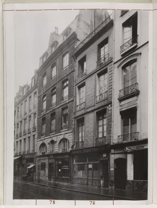 Schwarze und weiße Stadtstraße mit Gebäuden, Fenstern, Geländern, Namensschildern und einer Straße unten.