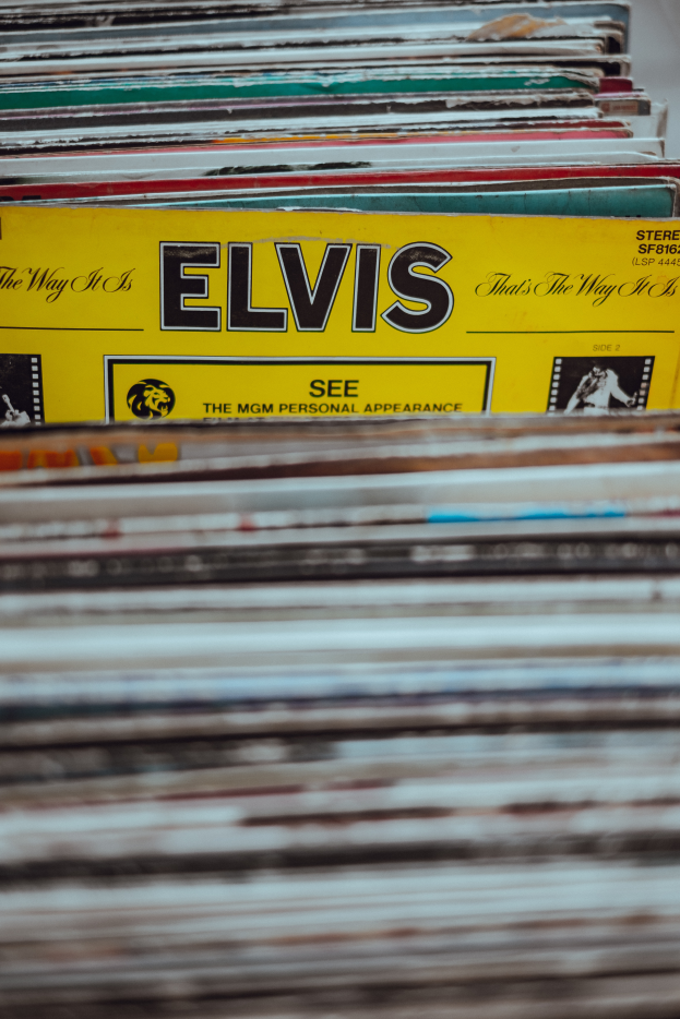 Ein ordentlicher Stapel Elvis-Presley-Platten auf einem Tisch, mit einigen Platten, die sich überschneiden und Titel sichtbar sind, vor einem leicht unscharfen Hintergrund.