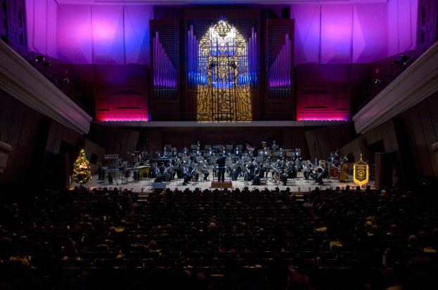 Ein voller Konzertsaal mit Zuschauern, Musikern auf der Bühne und einem Weihnachtsbaum im Hintergrund.