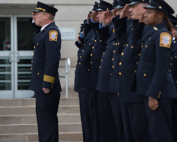 Gruppe von Polizisten in Uniform, die in Formation salutieren vor einem Gebäude mit Glastüren und Treppe.