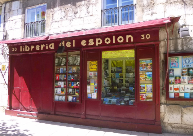 Eine Buchhandlung mit rotem Schirm namens "Libreria del Espolon" mit ordentlich sortierten Büchern, die durch ihre Fenster sichtbar sind.