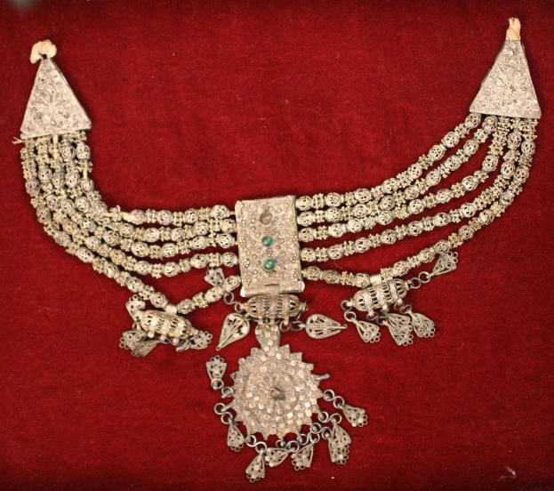 Silberne Kette mit Smaragden und Diamanten auf einem roten Samt-Hintergrund.