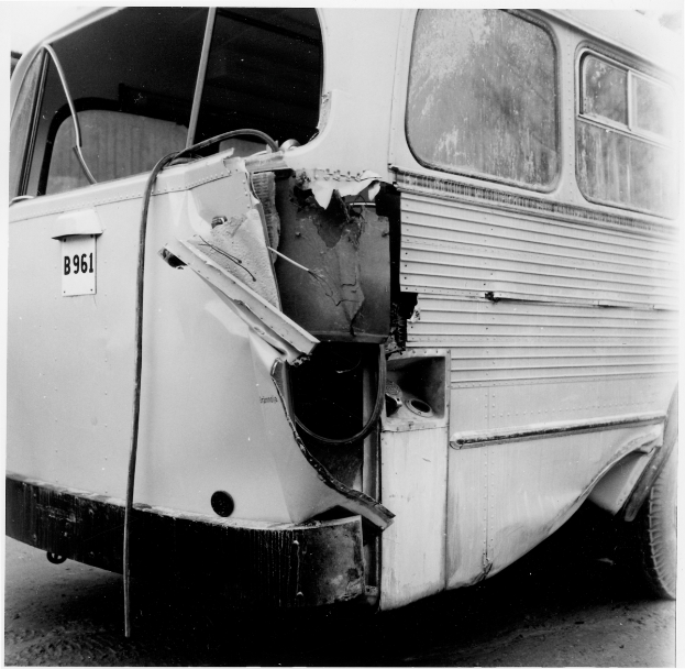 Ein Schwarz-Weiß-Foto eines beschädigten Busses auf der Straße, mit schwerer Frontschädigung durch einen Autounfall.