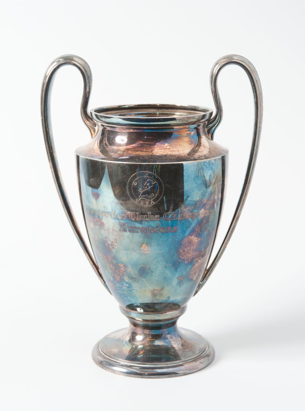 UEFA Champions League-Trophäe, ein stählerner Pokal mit zwei Griffen und einem blauen und silbernen Farbschema, mit der Inschrift "UEFA Champions League" auf einem weißen Hintergrund.