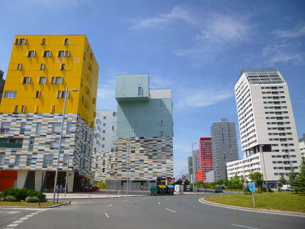 Eine Stadtstraße mit hohen Gebäuden, die als Teil der Universität Rotterdam bezeichnet sind, Straßenlaternen, Straßenschilder, Kraftfahrzeuge, Informationsanzeigen, Büsche, Bäume und eine bewölkte Himmel.