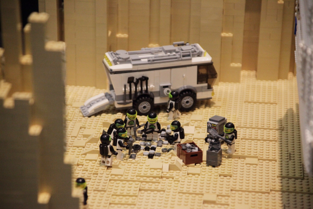 Lego-Modell einer Star-Wars-Szene mit einem Landfahrzeug im Vordergrund und einer Wand im Hintergrund sowie einigen verstreuten Lego-Spielzeugen.