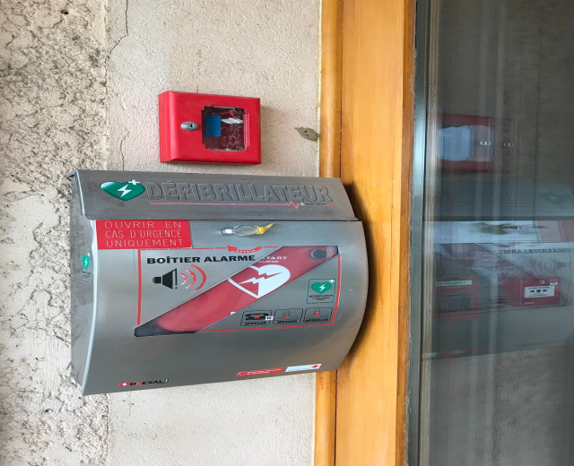 Rote Feueralarmanlage (Defibrillator) an der Seite eines Gebäudes neben einer Glastür montiert.