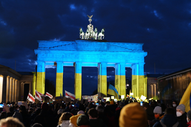 Menge mit Fahnen und Plakaten vor dem Reichstagsgebäude in Berlin, mit einer Banner auf der rechten Seite.