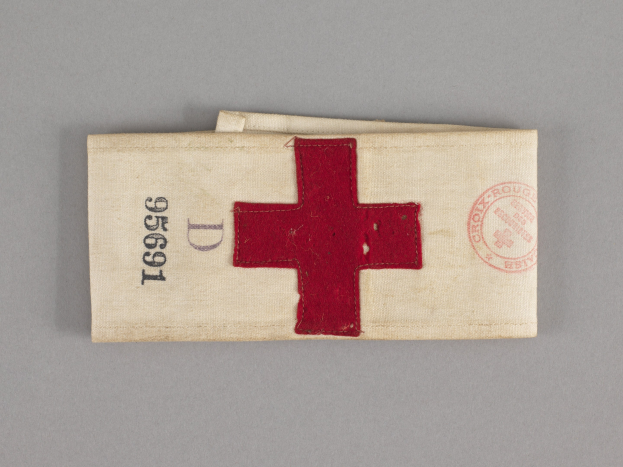 Ein rotes Kreuz-Erste-Hilfe-Set in einer Stofftasche mit Text und einem Stempel, das auf einer Oberfläche liegt.