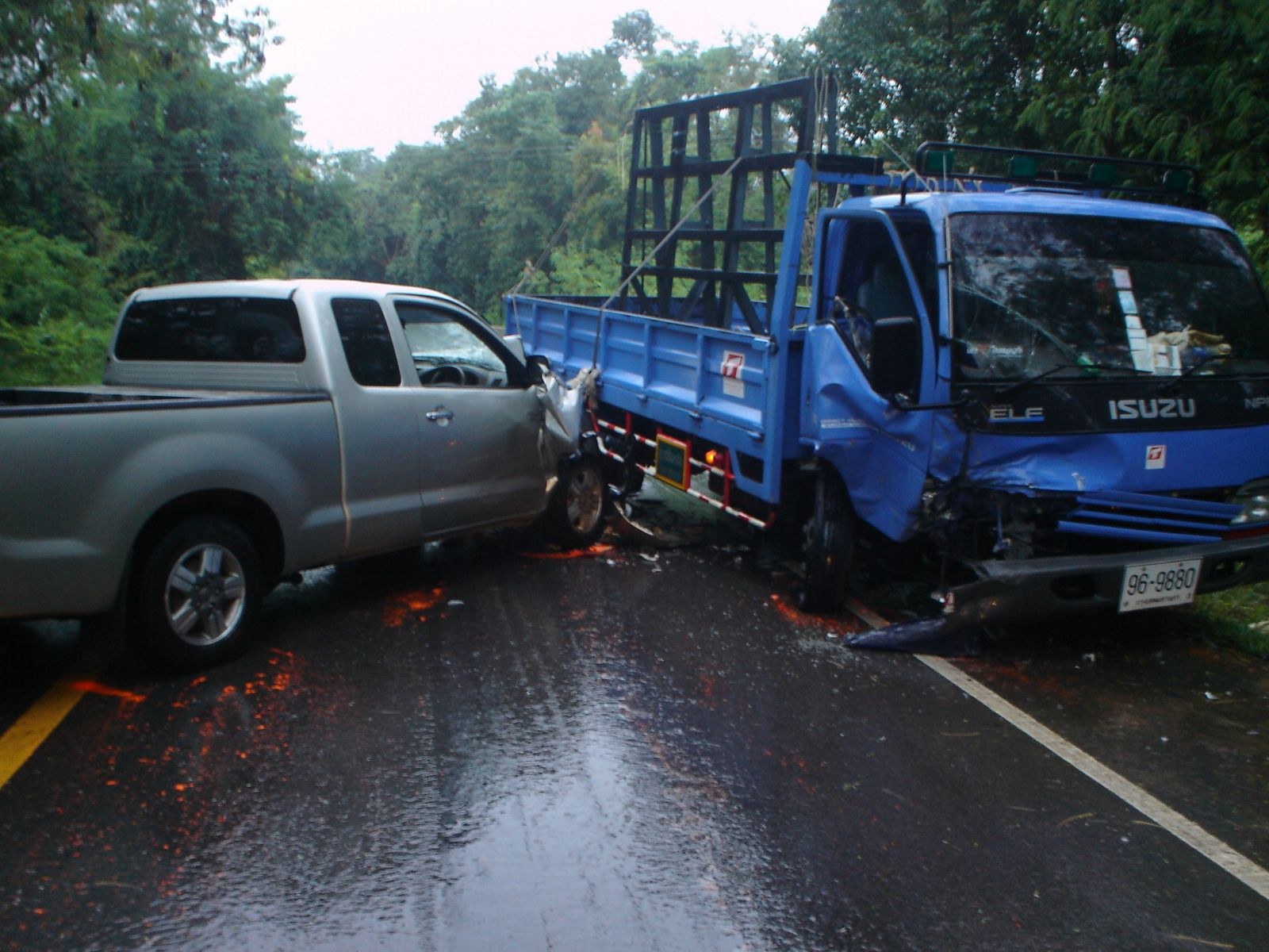 Ein beschädigter Lkw mit eingedellter Front und verbeulter Karosserie am Straßenrand, umgeben von Bäumen unter einem klaren blauen Himmel.