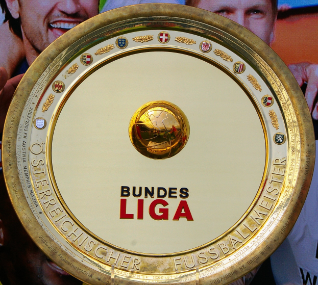 Goldener Schild mit "Bundesliga"-Text in der Hand eines Mannes, im Hintergrund ein Banner mit drei Personen.