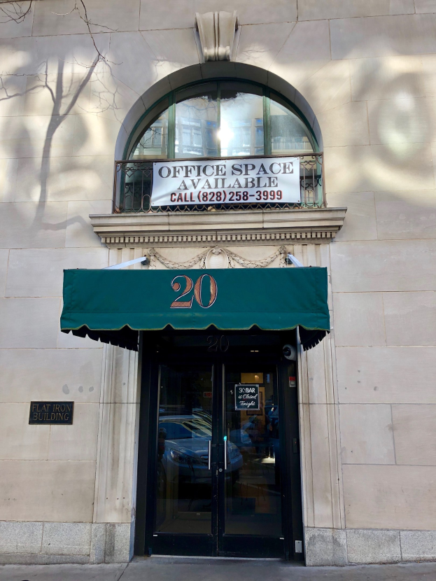 Glasstür mit einem grünen Vordach an einem Gebäude, das ein Schild trägt, das "Büroräume verfügbar" anzeigt, ein Geländer und einen Baum links.