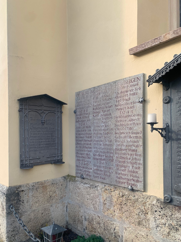 Ein Gebäude mit einer Holocaust-Gedenktafel, einem Fenster, einer Tür, einer Leuchte, einer Kette und Topfpflanzen.
