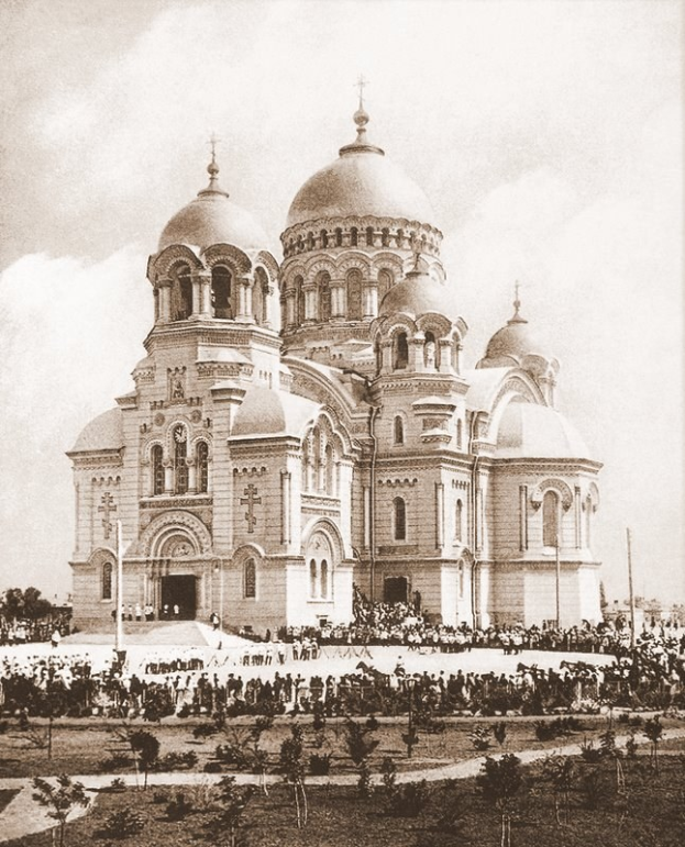 Schwarz-weiß-Fotografie der Erlöserkirche am Bluteigenen Fels in St. Petersburg, Russland, mit Menschen drumherum, Bäumen und Pfählen im Vordergrund und Text unten.