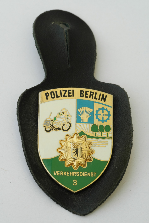 Ein Berliner Polizeischild mit einem blauen Schild, weißer Umrandung, einem zentralen weißen Stern und schwarzer Schrift 'Polizei Berlin' in fetter Schrift, das auf einer Oberfläche ruht.
